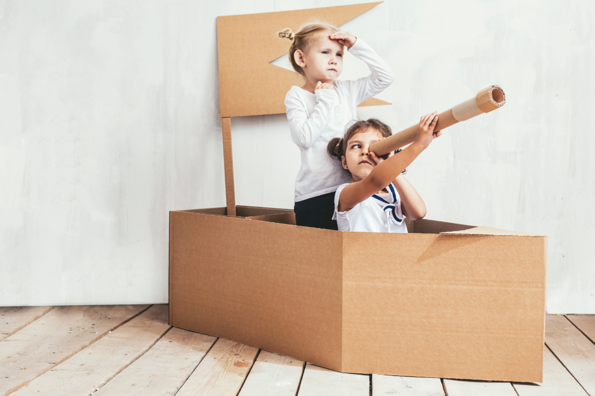 Enfants jouant dans un bateau en carton fabriqué à partir d’une grande boîte, jeu d’imagination sans écran à la maison.