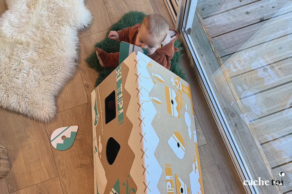 Vue d'ensemble d'une cabane tipi en carton recyclé s'intégrant dans un salon chaleureux, démontrant le design narratif et l'esthétique éco-responsable de la marque.